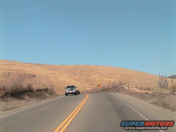 White pickup truck on a two-lane road, with a dark car behind it