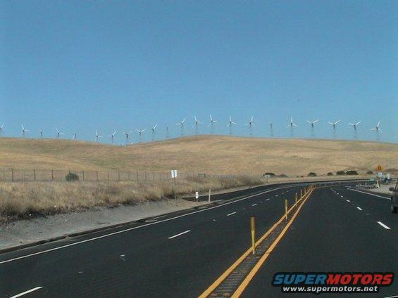 Highway with wind turbines on a distant hill under a clear blue sky