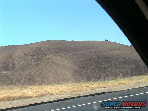 Distant dark vehicle on a brown, grassy hill under a clear blue sky