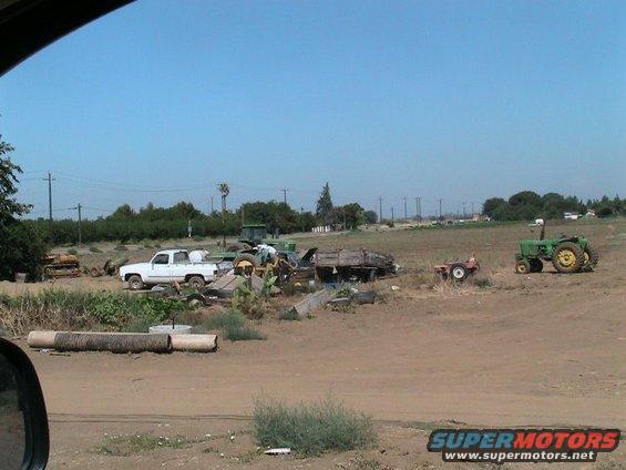 White pickup truck and several tractors in a dry, open field under a clear blue sky