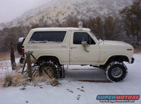 White Ford Bronco with lifted suspension and spare tire on rear, parked in snow