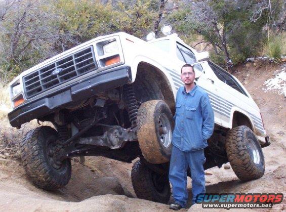 White lifted off-road SUV with a man standing next to it, showing its suspension and tires