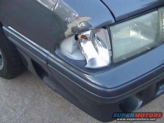 Front corner of a dark blue 1989 Ford Mustang with a broken headlight assembly