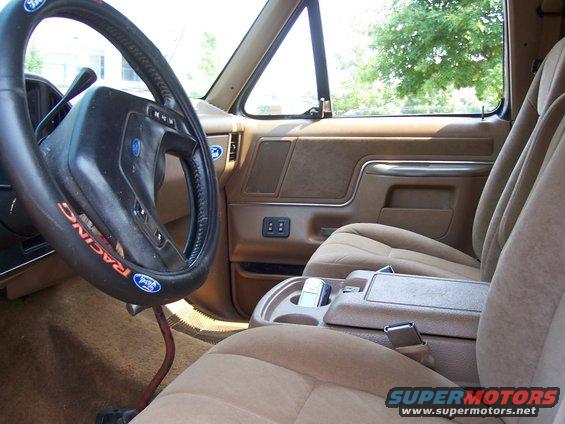 Interior shot of a truck's driver side, showing the steering wheel, dashboard, and passenger seat. Steering wheel has a 'Racing' cover