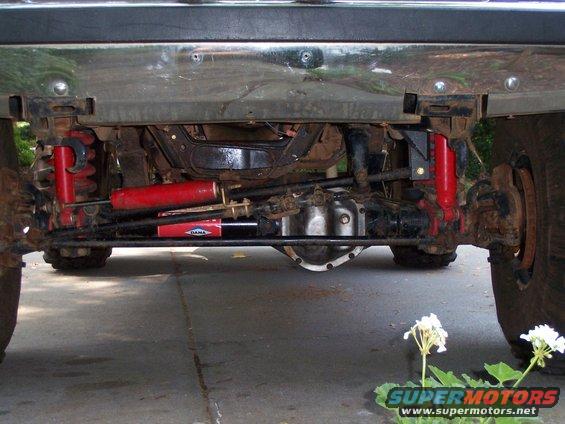 Undercarriage view showing front axle, red shocks, and steering components. "DANA" visible on a shock
