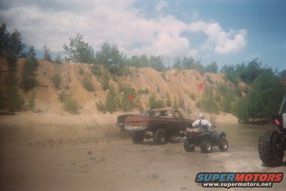 Brown pickup truck and ATV on sandy terrain with red flags