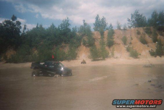 Black pickup truck with a red flag on top, partially submerged in muddy water