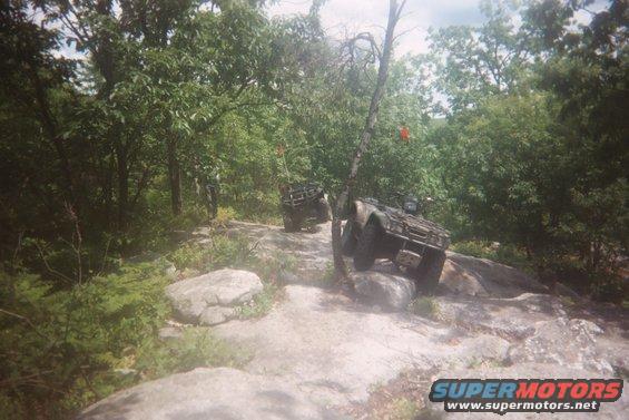 Two ATVs navigating a rocky, wooded trail