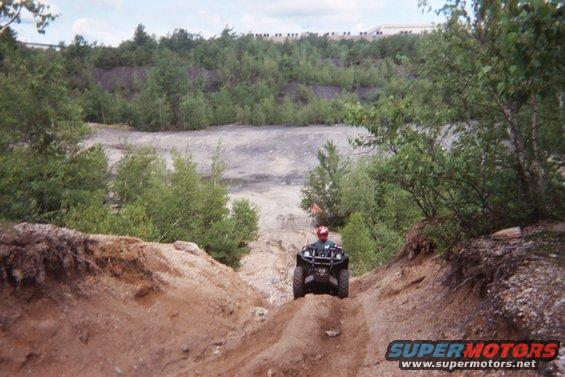 Black all-terrain vehicle with a rider wearing a red helmet descending a dirt path