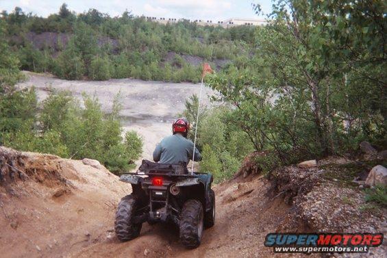 ATV riding on a dirt path in a wooded, rocky area. Person wearing a red helmet