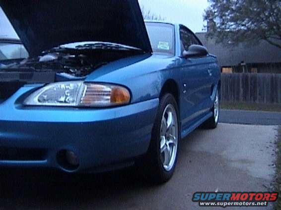 Blue Ford Mustang, front quarter view, hood open, showing engine bay. Aftermarket wheels visible