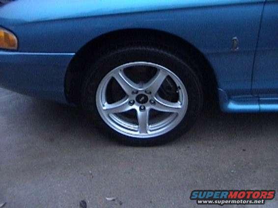 Blue car side view showing aftermarket wheels and fender emblem