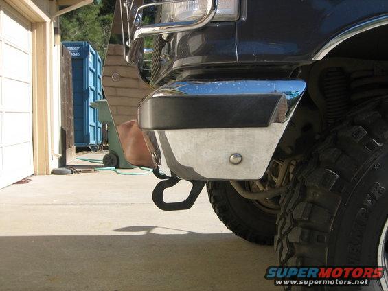Dark colored truck's chrome bumper with tow hook, large tire visible