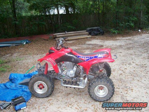 Red ATV parked on dirt ground with blue tarp and toolbox nearby