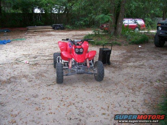 Red ATV parked on a dirt lot with trees in the background