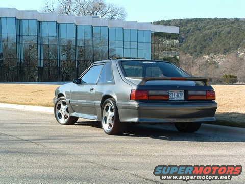 Silver coupe with a rear spoiler and aftermarket wheels parked on asphalt
