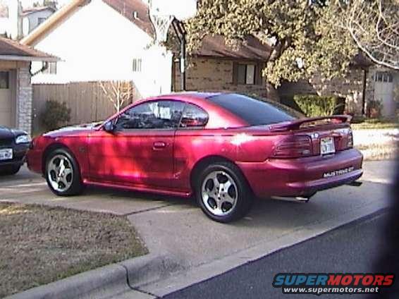 Red coupe parked on driveway, rear quarter view. "MUSTANG GT" text visible on rear bumper