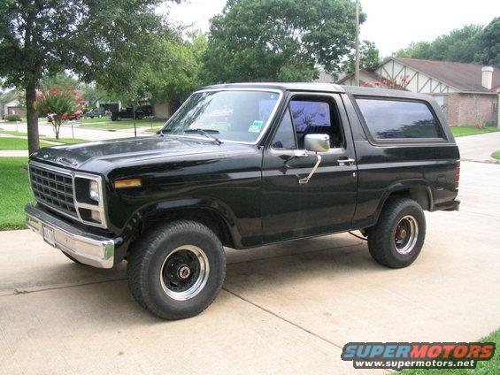 Black 1980s Ford Bronco parked on a driveway, viewed from the front three-quarter angle