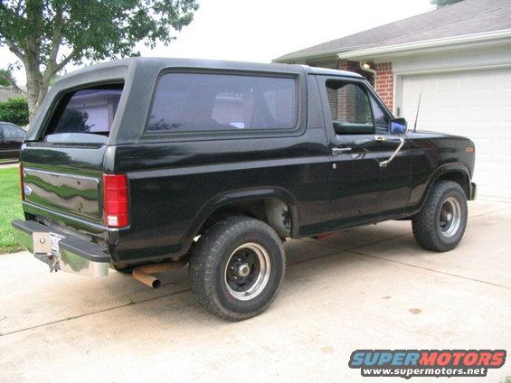 Black Ford Bronco parked in driveway, side view. Has aftermarket wheels and tinted windows