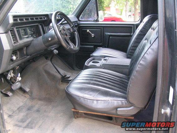 Black vinyl seats and dashboard of a truck, with a floor shifter and aftermarket steering wheel