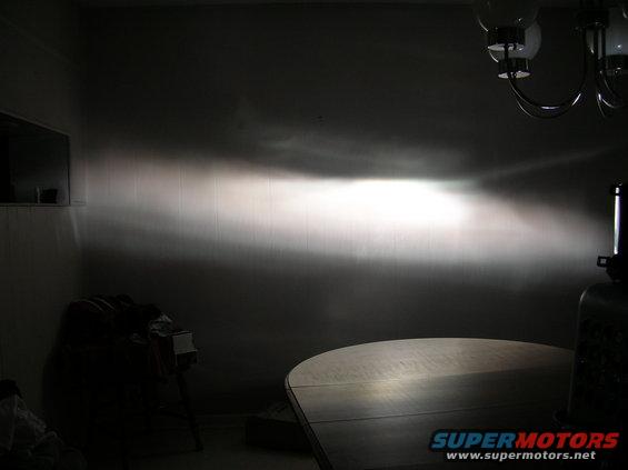Headlight beam pattern projected onto a wall, with a table in the foreground and a chandelier above