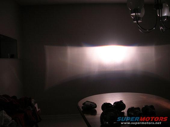 Headlight beam pattern projected onto a wall, with a chandelier visible in the upper right