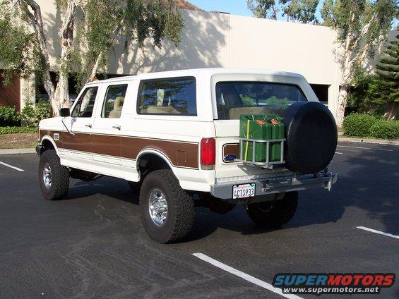 White Ford Bronco Centurion Conversion with brown woodgrain trim, spare tire, and jerry cans on rear bumper
