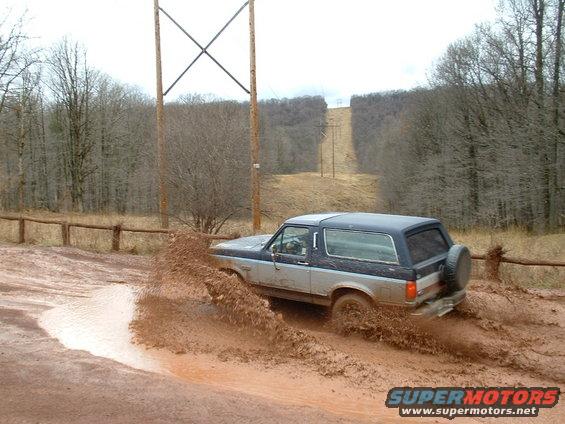 Two-tone SUV driving through mud, kicking up a large spray