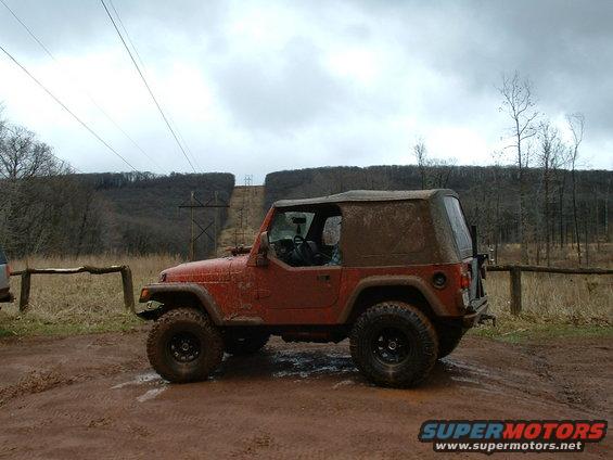 Red Jeep Wrangler parked on a muddy trail with trees and power lines in the background