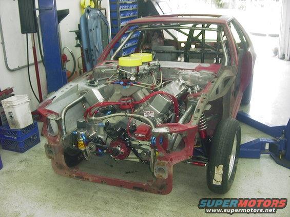 Custom race car with engine exposed, roll cage visible, in a workshop