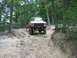 1992 Ford Mustang - A lifted pickup truck navigates a challenging off-road path through a forest.
