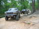 1992 Ford Mustang - A lifted 1992 Ford F-Series truck leads a line of off-road vehicles on a wooded trail.