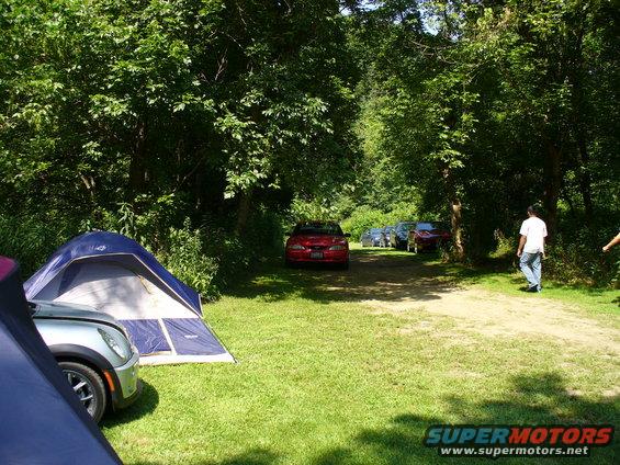 Red car parked on dirt road with tents and trees