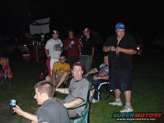 Group of men gathered outdoors at night, some holding drinks