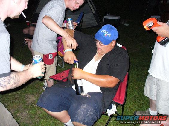 People gathered outdoors at night, one opening a bottle
