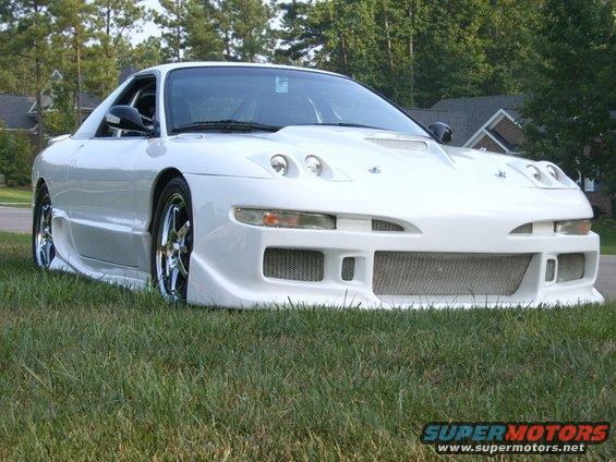 White sports car with aggressive front bumper, side skirts, and hood scoop parked on grass