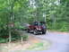 1995 Ford C-350 (Centurion Conversions) - A brown Jeep Wrangler is parked on a paved road in a wooded area, with a maroon SUV behind it.