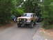 1995 Ford C-350 (Centurion Conversions) - A tan Ford Bronco with custom smiley face lights on its grille guard is parked on a paved road, with another vehicle behind it.