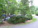 1995 Ford C-350 (Centurion Conversions) - A dark blue pickup truck with a white camper shell is parked amongst trees and bushes at a campsite.