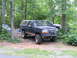 1995 Ford C-350 (Centurion Conversions) - A lifted blue Ford Bronco is parked in a wooded area with another truck nearby.