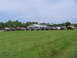 1995 Ford C-350 (Centurion Conversions) - A group of off-road vehicles are parked in a grassy lot in front of a building and gas station.