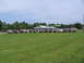 1995 Ford C-350 (Centurion Conversions) - A collection of trucks and SUVs are gathered in a field, with a gas station and trees in the background.