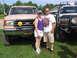 1995 Ford C-350 (Centurion Conversions) - A couple poses in front of a lifted tan Ford F-Series truck and a white Ford F-Series truck with a "FOR SALE" sign.