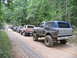1995 Ford C-350 (Centurion Conversions) - A line of off-road vehicles, including a Ford Bronco, travel down a dirt path in a wooded area.