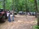 1995 Ford C-350 (Centurion Conversions) - A group of off-road vehicles are parked in a wooded area, with several people standing around them.