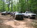 1995 Ford C-350 (Centurion Conversions) - A group of off-road vehicles are parked on a dirt trail surrounded by trees.