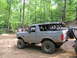 1995 Ford C-350 (Centurion Conversions) - Modified SUV with large tires parked on a dirt trail surrounded by trees.