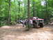 1995 Ford C-350 (Centurion Conversions) - Several people gather around a heavily modified red pickup truck in a forest clearing.