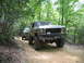 1995 Ford C-350 (Centurion Conversions) - Two off-road vehicles drive down a wooded trail in the summer.