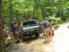 1995 Ford C-350 (Centurion Conversions) - A group of men gather around a Ford Bronco on a wooded off-road trail.